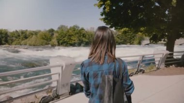 Yavaş hareket kamera Niagara Falls azgın su akışına yürümek çanta ile rahat giysiler içinde mutlu yerel kadın takip.