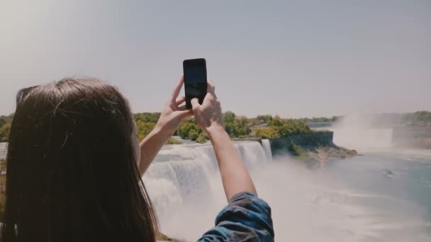 スローモーションカメラスライドは、興奮した若い観光客の女性は、驚くべきナイアガラの滝ビューの携帯電話の写真を撮って後ろに残さ. — ストック動画