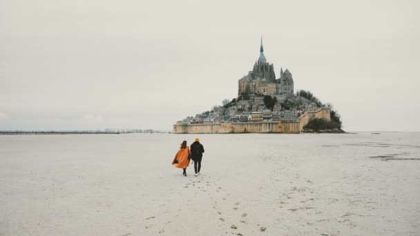Hermoso rodaje cinematográfico, drone sigue joven pareja feliz caminando hacia Mont Saint Michel fortaleza en Normandía Francia — Vídeos de Stock