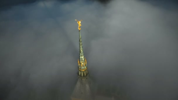 Primer plano aéreo atmosférico de estatua dorada brillante en la cima del campanario del castillo del Mont Saint Michel sobre nubes oscuras . — Vídeo de stock