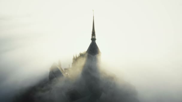 Luftaufnahme, Nebelschwaden, die während des epischen Sonnenaufgangs in der Normandie über die berühmte majestätische Mont Saint Michel Festung hinwegziehen. — Stockvideo