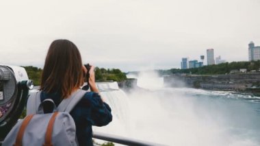 Sırt çantası ve kamera inanılmaz Niagara Falls şelale yavaş hareket fotoğraf çekerken mutlu gezgin kadının arka görünümü.