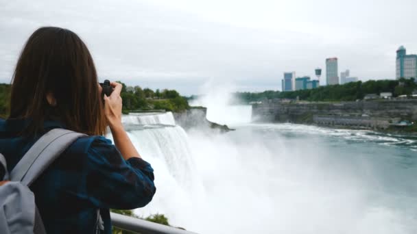 Tillbaka syn på upphetsad journalist kvinna med kamera ta foto av episka Niagara Falls, ser runt leende slow motion — Stockvideo
