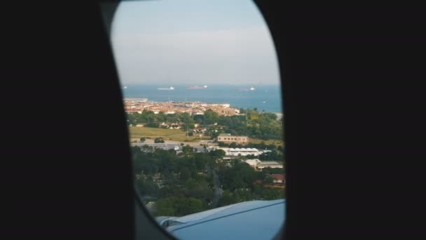 Avión está aterrizando sobre hermosa ciudad soleada junto al mar verano, increíble vista de la ciudad y el ala a través de la ventana del avión . — Vídeos de Stock