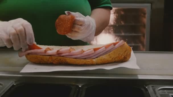 Процес виготовлення великого бутерброда королівського розміру з шинкою та салямі. Руки людини викладають інгредієнти на великий хліб . — стокове відео