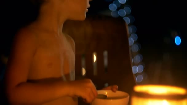 Cámara inclina hacia abajo en el niño feliz comer postre con cuchara grande en la noche exótica bar salón de playa con luces bokeh — Vídeos de Stock