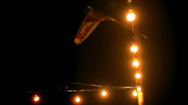 Belle prise de fond de lumières atmosphériques de nuit patio extérieur string, grand drapeau du Sri Lanka agitant dans le vent léger . — Video