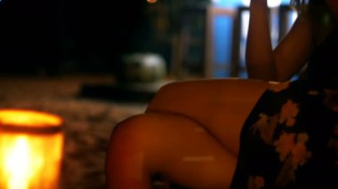 Yakın çekim kamera, akıllı telefon kullanarak bacaklı gece lounge beach bar sandalyesinde oturan mutlu genç kadın üzerinde eğilir