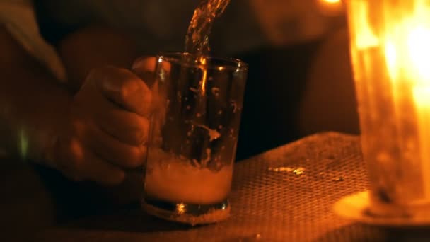 在夏季夜间海滩休息室，人类手将泡沫汽水饮料倒入桌上的玻璃杯中，桌上配有蜡烛的特写镜头 — 图库视频影像