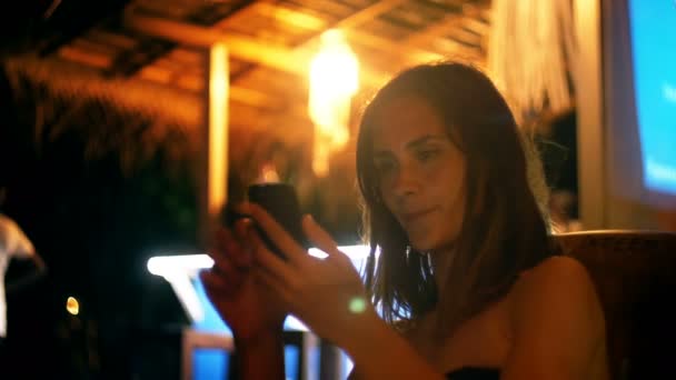 Feliz relajado joven mujer caucásica utilizando la aplicación de entretenimiento smartphone en la cafetería salón de noche atmosférica de vacaciones . — Vídeo de stock