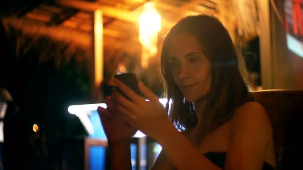 Feliz joven mujer de negocios sonriente usando aplicación de mensajero smartphone en línea en la noche de verano salón cafetería en vacaciones . — Vídeo de stock