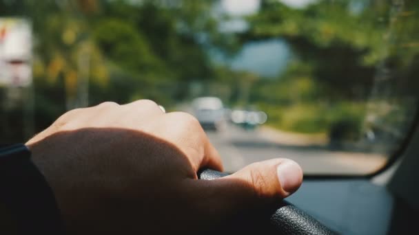 Hermoso primer plano en el coche, mano masculina sosteniendo el volante conduciendo a lo largo de borrosa hermosa carretera soleada con árboles verdes . — Vídeos de Stock