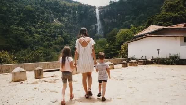 Camera segue felice giovane madre con due bambini che camminano verso incredibile vista cascata della giungla in Sri Lanka rallentatore . — Video Stock