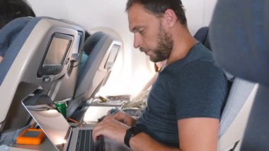 Akıllı saati olan genç odaklı yaratıcı işadamı uçak yolculuğu sırasında laptop mobil ofisinde çalışıyor..