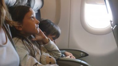 Aile ile birlikte tatile giden uzun uçak uçuşu sırasında etrafa bakan iki küçük sıkılmış çocukların yan görünümü.
