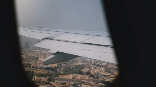 Hermosa vista detrás del ala del avión desde el asiento de la ventana después de despegar, avión volando por encima de la hermosa ciudad costera soleada . — Vídeo de stock