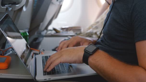 Primer plano joven empresario freelance con reloj inteligente utilizando el ordenador portátil para trabajar en línea durante el vuelo de viaje de negocios del avión . — Vídeos de Stock