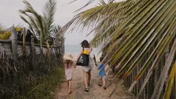 Feliz familia joven, madre con hijo pequeño e hija, caminando juntos hacia la hermosa playa del océano de vacaciones . — Vídeos de Stock