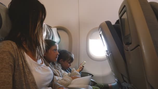 Side view of young beautiful mother with two little bored kids during long airplane flight going to vacation together. — Stock Video