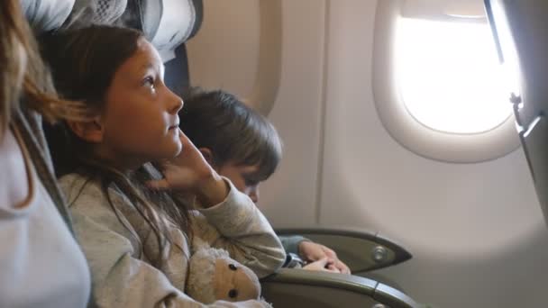 Vista lateral de dos niños aburridos mirando a su alrededor durante el vuelo largo del avión que va a vacaciones junto con la familia . — Vídeo de stock