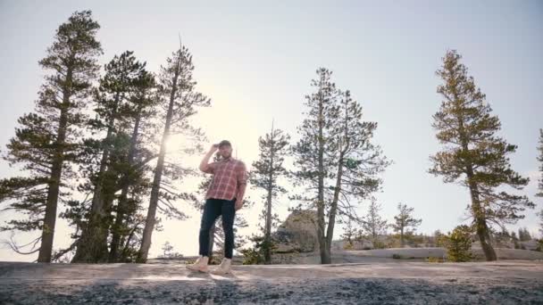 Дивовижний низький кут пострілу молодий чоловік стояв один на великий рок з сонцем підсвічування спалаху в Yosemite парку повільний рух. — стокове відео