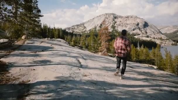 Kamera Yosemite dağ gölü yavaş hareket tek başına yürüyüş sırasında büyük kayalar aşağı çalışan genç mutlu turist adam izler. — Stok video