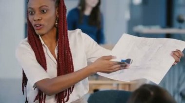 Mutlu profesyonel Afro-Amerikan mimar iş kadını modern ışık ofis ortakları için proje sunan.