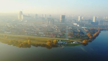 Drone büyük günbatımı şehir sahne üzerinde uçan, güzel hala göl kıyısı ve sarı sonbahar ağaçları yakın çeşitli binalar.