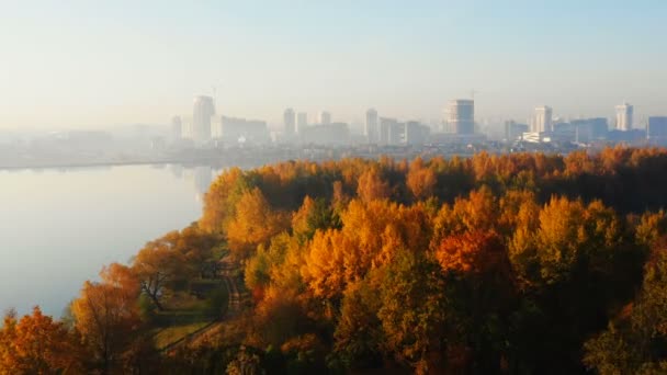 Drohne bewegt sich zu wunderschönem Sonnenaufgang Stadtsilhouette Panorama über stille See Wasser und sonnigen gelben Herbstwald. — Stockvideo