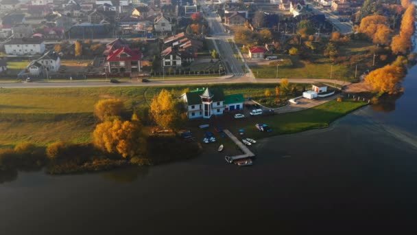 Drone se překlání nad krásným velkým domem s molo a čluny poblíž břehu jezera a podzimních stromů při západu slunce. — Stock video