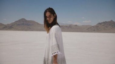 Kamera kamera bakarak ve Utah Salt Desert gölünde açık kollar ile dönen güzel genç mutlu kadın izler.