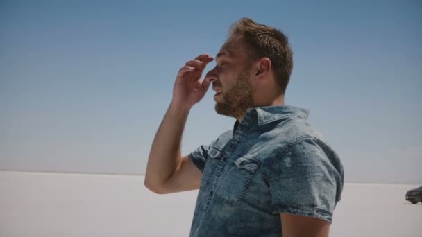 Close-up shot of young tired man in casual clothes lost, looking around in the middle of hot dry salt lake desert Utah. — Stock Video