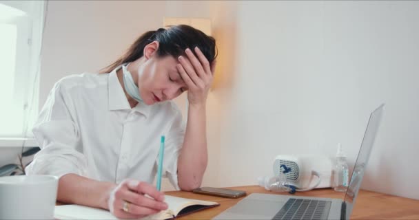 漂亮而疲惫的30多岁的白人医生，一位疲惫不堪的妇女，在家里工作，用笔记本电脑给病人看病. — 图库视频影像