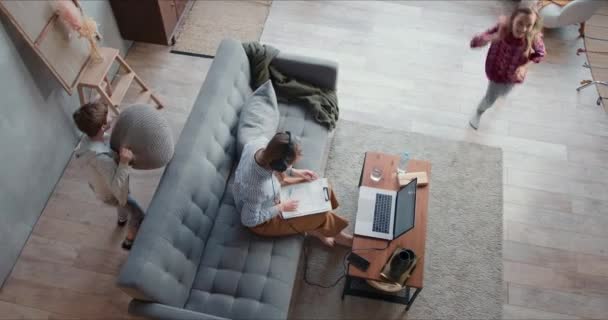 Top view twee tiener kinderen maken hun jonge moeder gek terwijl ze probeert te werken van thuis uit online met behulp van laptop. — Stockvideo