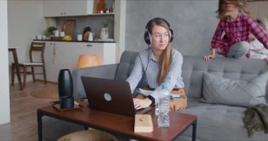 Genç, mutlu, beyaz bir anne iki gürültücü çocukla evde laptopla çalışırken dikkati dağılıyor..