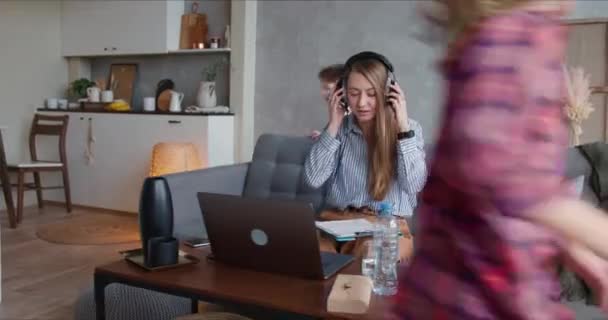 Tecrit sorunları. İki genç çocuk etrafta koşuşturuyor, laptopla evden çalışmaya çalışan beyaz bir annenin dikkatini dağıtıyor.. — Stok video