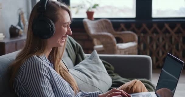 Trabajando desde casa en auto aislamiento. Feliz joven rubia se ríe utilizando la videollamada portátil para el trabajo en línea . — Vídeos de Stock