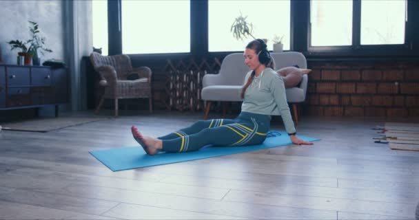 Linda jovem loira magro fazendo ioga alongamento treino com aplicativo de telefone inteligente e fones de ouvido no tapete em casa . — Vídeo de Stock