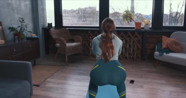 Vista trasera atlética mujer joven haciendo ejercicio de fitness ejercicios en cuclillas en la esterilla de yoga en casa en cuarentena de autoaislamiento . — Vídeo de stock