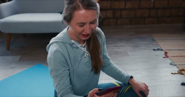 Evde karın kası egzersizi yapan güzel bir kadın akıllı telefon uygulaması kullanarak spor koçuyla internetten konuşuyor.. — Stok video