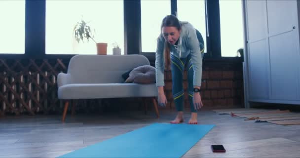 Giovane sportiva bella donna caucasica sottile che si estende a casa prima dell'allenamento di yoga per mantenere in buona salute durante la quarantena . — Video Stock