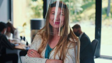 İş yeri güvenlik önlemleri. Ofiste ağır çekimde plastik yüz maskesi takan mutlu bir iş kadınının portresi..