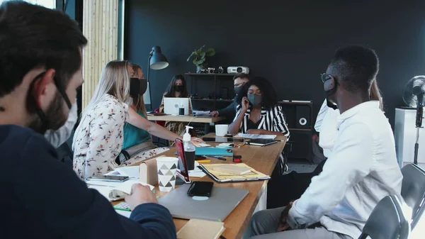 Seguridad en la oficina durante el COVID-19. Jóvenes empresarios multiétnicos y serios trabajan juntos en reuniones con máscaras faciales. —  Fotos de Stock