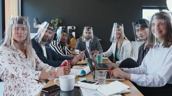 Reuniões de negócios durante o COVID-19. Equipe de negócios diversa feliz ouvindo, batendo palmas para a câmera, todos vestindo escudos faciais. — Fotografia de Stock