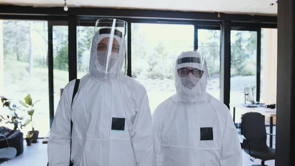 Zoom in on two male healthcare workers wearing full white disposable medical suits with face shields during COVID-19.