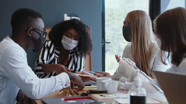 Happy multiethnic development company business people consulting customers at light office table wearing face masks.