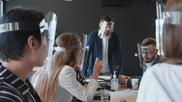 Biztonságos munkahely a COVID-19 lezárása után. Boldog többnemzetiségű üzletemberek csapata visel arc pajzsot az irodai találkozón. — Stock Fotó