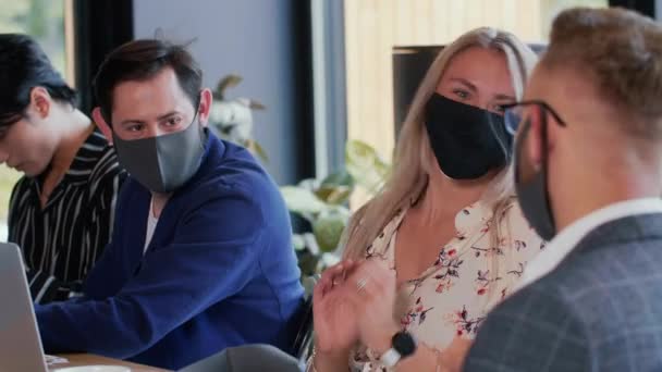 COVID-19 seguridad en el lugar de trabajo. Jóvenes empresarios felices trabajan juntos en una reunión de mesa con máscaras faciales pandémicas. — Vídeos de Stock