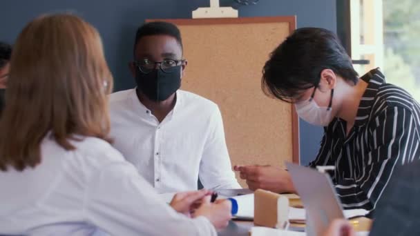 Las máscaras pandémicas como una nueva normalidad. Feliz joven empresario negro activamente gestos en el encuentro con compañeros de trabajo multiétnicos. — Vídeo de stock