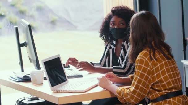 工作场所的医疗安全。两位漂亮、快乐的多民族女商人戴着面具在办公室里共事. — 图库视频影像